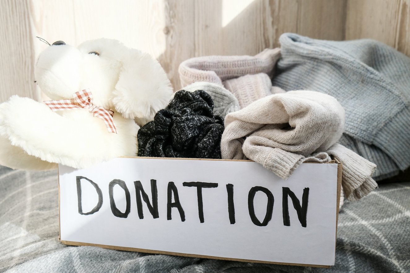 Donation Box with Old Used Toys and Clothes Indoors. Happy Charity. Box with Clothes in It. Close-up. Clothing Donation. Winter Clothes in a Cardboard Box.